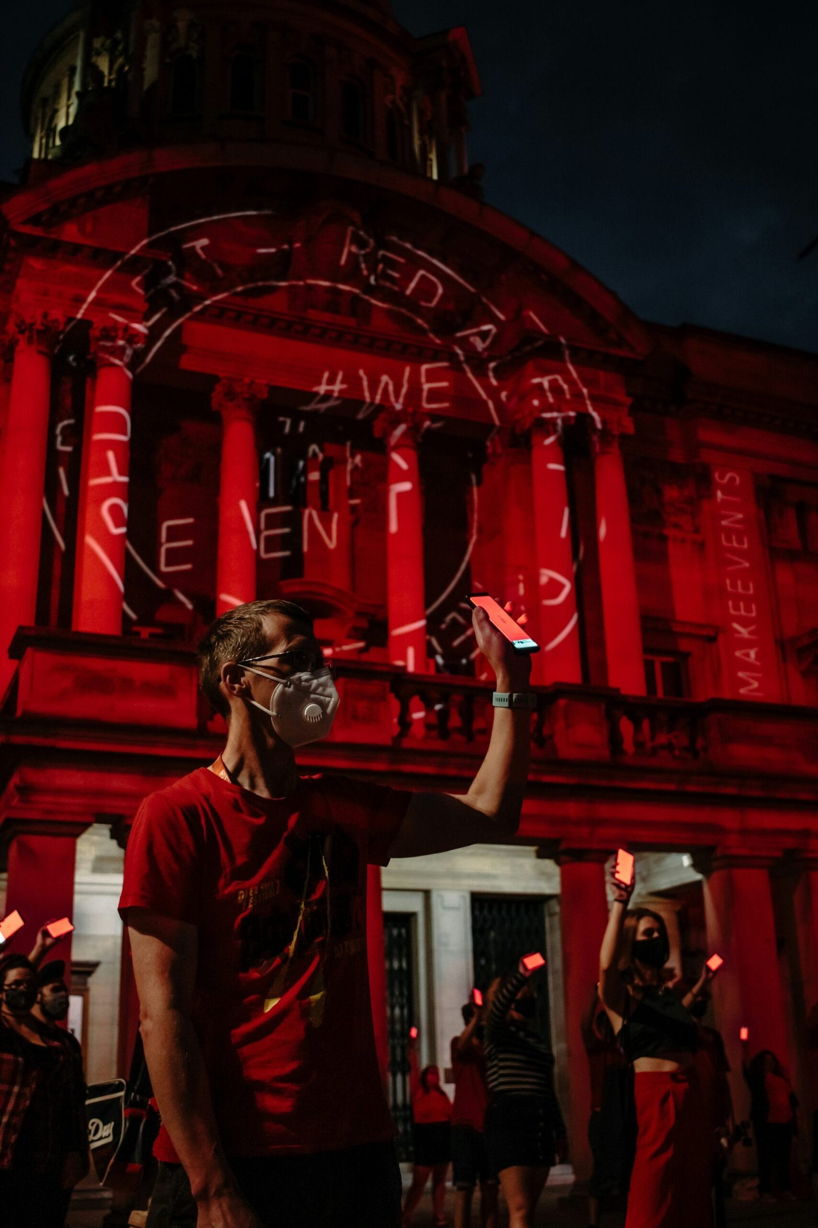 man in white crew neck t-shirt wearing black goggles standing near red building during nighttime